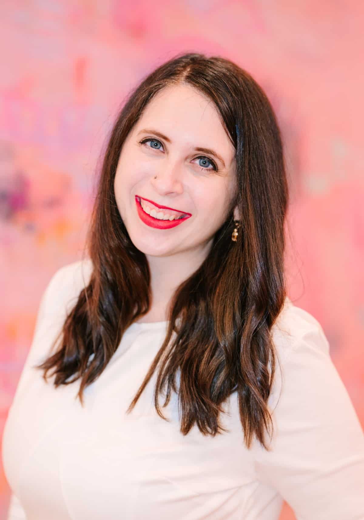 Cait Potter smiling in a white top against a pink backdrop